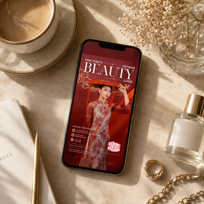 A smartphone lying on a beige tabletop, displaying a red magazine-style cover titled 'Beauty Guide' with Tina Vonci and Vietnam text. The scene is styled with a cup of coffee, dried flowers, a notebook, a pen, a ring, and a perfume bottle around it.