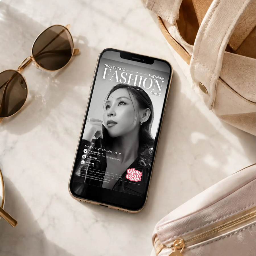 A smartphone lying on a light marble surface, displaying a fashion magazine cover on its screen. The scene is styled with round sunglasses, a cup of coffee on a saucer, and beige handbags in a bright, sunlit setting.