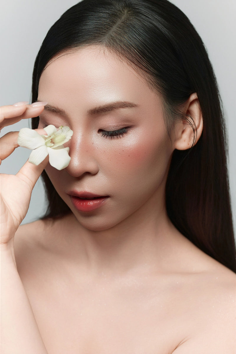 Woman holding a white flower near her face against a plain background